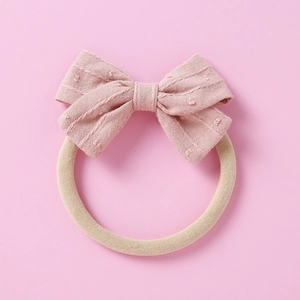 Close-up of pink jacquard bow with textured dots on a soft beige baby nylon headband