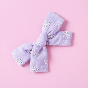 Detailed close-up of a purple cotton lace hair bow with delicate white floral embroidery