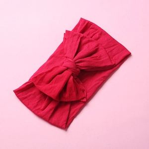 Close-up of vibrant red soft nylon bow headband for infants on pink background
