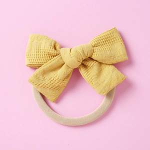 Vue détaillée d'un chouchou nœud jaune avec motif gaufre sur un fond rose pastel