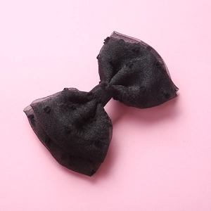 Gros plan d'une pince à cheveux en tulle noir avec pois 3D et nœud multicouche sur fond rose