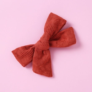 Macro shot of dark brick red bow hair clip with intricate mesh texture and floral pattern