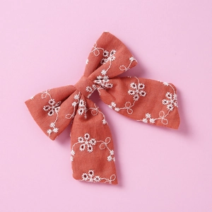 Détail de la pince à cheveux en coton rouge rouille avec broderie florale blanche fine