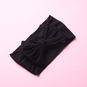 Close-up of soft black nylon baby headband with a large bow detail on pink background
