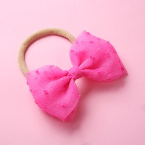 Détail d'un nœud en résille rose à pompons sur un bandeau de bébé en nylon doux sans couture