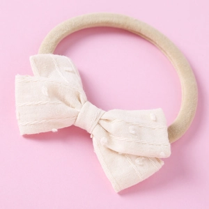 Detailed close-up of cream jacquard bow baby headband with soft brown nylon elastic band