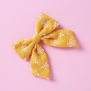 Détail d'un nœud papillon en coton jaune avec broderie florale blanche et texture