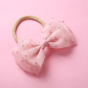 Détail d'un bandeau en nylon pour bébé avec un grand nœud en tulle rose à pois