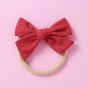 Détail d'un nœud en coton rouge texturé sur un bandeau élastique pour bébé en nylon beige