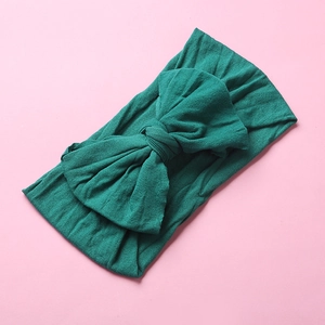Detail of soft dark green nylon bow headband for babies on a pink background