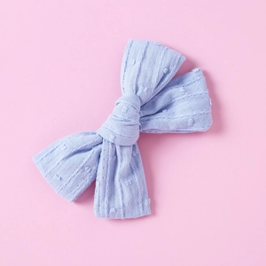Close-up of light blue cotton bow hair clip with textured polka dots on pink background