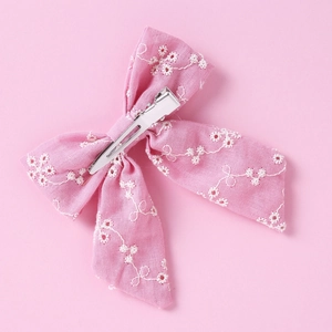 Détail d'une pince à cheveux rose en coton pour bébé avec broderie florale et clip métal