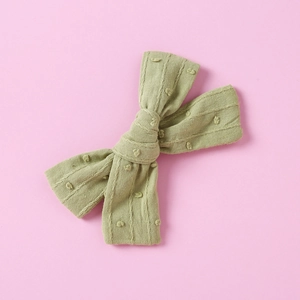 Close-up of baby hair clip featuring avocado green jacquard bow with raised polka dot textures