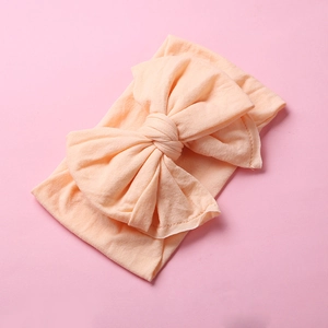 Detailed texture of peach nylon infant headband featuring a large soft swallowtail bow