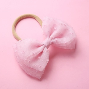 Détail du nœud en tulle rose à pois sur un bandeau bébé en nylon souple, fond rose