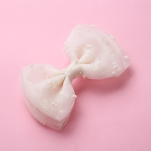 Détail d'une pince à cheveux avec nœud en tulle blanc à pois sur fond rose clair