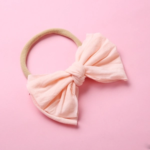 Détail du bandeau rose doux pour bébé avec un grand nœud en tissu moelleux sur fond rose