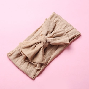 Detail of a soft beige nylon headband with a large bow for infants on a pink background