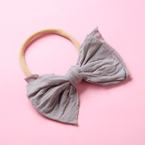 Détail du bandeau en nylon pour bébé avec un nœud gris tricoté sur fond rose