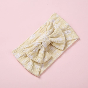 Gros plan d'un bandeau bébé en maille jaune avec motifs cœurs et un grand nœud