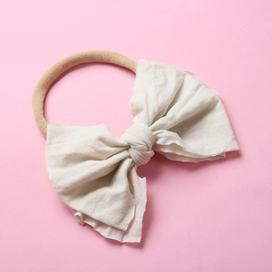 Détail du bandeau en nylon pour bébé avec nœud crème et bords ondulés élastiques