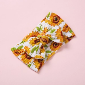Détail d'un bandeau pour bébé avec grand nœud et motif tournesol jaune sur tissu tricoté