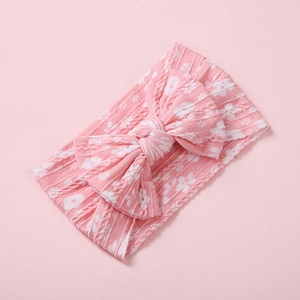 Gros plan du bandeau tricoté rose clair pour bébé avec grand nœud et motifs floraux blancs