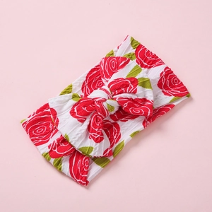 Détail d'un bandeau pour bébé avec imprimé rose rouge et gros nœud en tricot