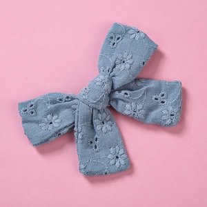 Détail de la pince à cheveux nœud bleu en dentelle de coton avec broderie florale sur fond rose