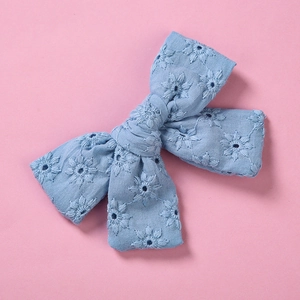 Détail d'une barrette noeud en coton bleu avec broderie délicate de marguerites blanches