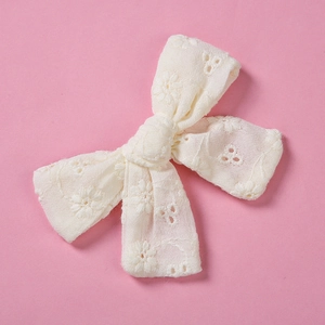 Détail de la pince à cheveux en dentelle crème avec broderie florale sur fond rose