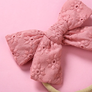 Detailed close-up of pink cotton bow headband with delicate floral embroidery and elastic band