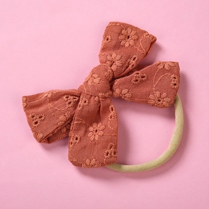 Detail of rust red cotton lace bow with floral embroidery on soft nylon headband