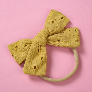 Detail of mustard yellow lace bow headband with daisy embroidery and soft nylon strap