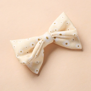 Détail de la pince à cheveux fleurie pour bébés avec motifs blancs sur tissu beige