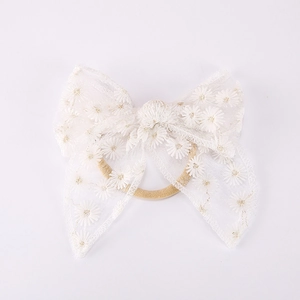 Détail du bandeau bébé avec grand nœud en dentelle blanche et broderie de marguerites
