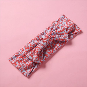Détail du bandeau élastique en tricot bleu à fleurs avec nœud papillon sur fond rose