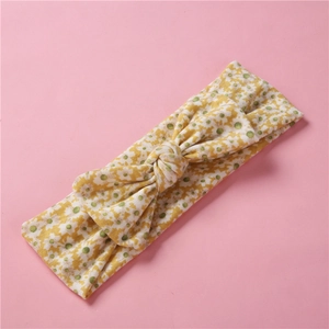 Détail d'un bandeau bébé à fleurs jaunes avec un grand nœud sur fond rose clair