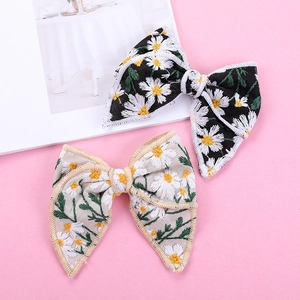 Barrettes à nœud brodées de marguerites en noir et beige sur un fond rose pastel