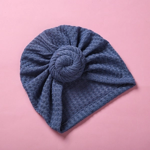 Detailansicht der blauen Waffelstrick-Babymütze mit Donut-Knoten auf rosa Hintergrund