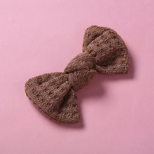 Détail d'un nœud papillon en laine tricotée marron foncé montrant la texture sur fond rose
