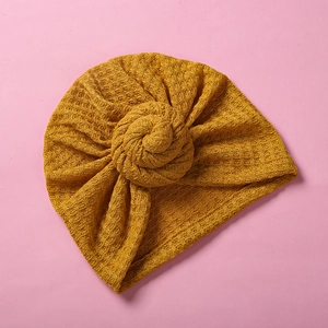 Detail einer Baby-Turbanmütze aus Waffelstrick in Senfgelb mit einem Haarknoten