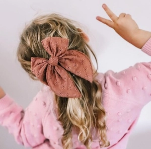 Detail of child wearing oversized maroon bow hair clip with floral embroidery