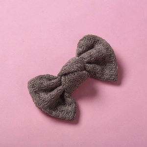 Gros plan d'une barrette nœud en tricot gris foncé avec texture laine sur fond rose