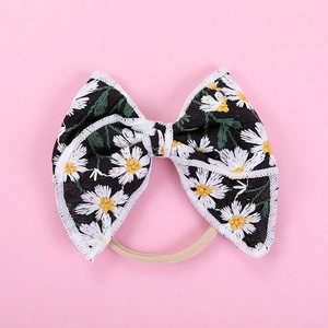Close-up of embroidered daisy pattern on black fabric bow with a nylon hairband