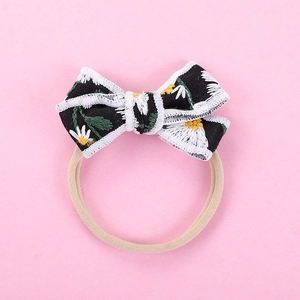 Detail of embroidered daisy pattern on black bow headband with soft nylon band