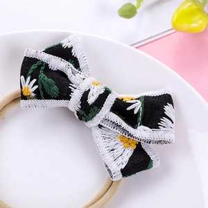 Detailed close-up of a black cotton bow headband with white daisy floral embroidery