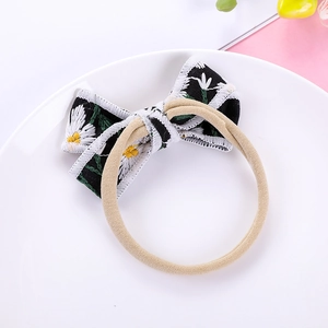Detail of white daisy embroidery on black cotton bow with soft nylon hair band