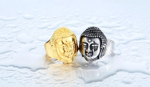 Macro view of gold and silver Buddha head rings on a textured water droplet surface