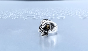Makroaufnahme des Punk-Totenkopfrings mit Silber-Finish und goldenem Akzent auf blauem Grund
